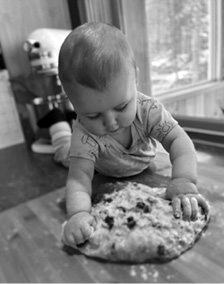 Amos, a young child, pressing his hands into a flattened round of bread dough